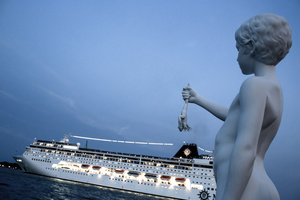 Charles Ray\'s sculpture The Boy with a Frog stands on the very tip of the Punta della Dogana in Venice while a large cruise ship passes through the Grand Canal. Heavy traffic of these large ships is believed to cause deterioration of the biodiversity of the lagoon, because large ships displace a lot of water, cause waves that destroy the salt marshes and wash away the soil.