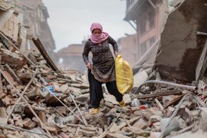 A woman wearing a scarf for protection from the dust salvages belongings from a family home that was destroyed during the 2015 Nepal earthquake.